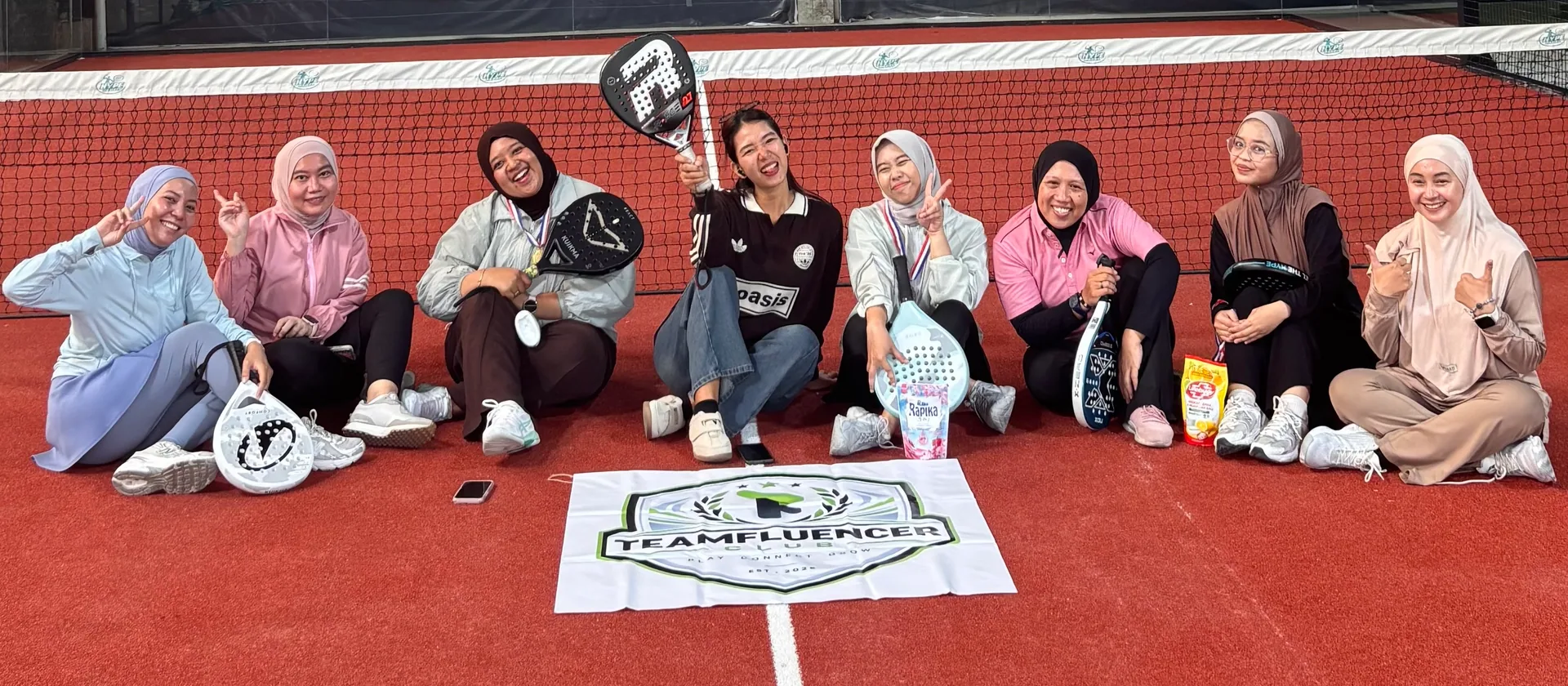 Peserta Teamfluencer Club duduk bersama dengan raket padel di tepi lapangan.